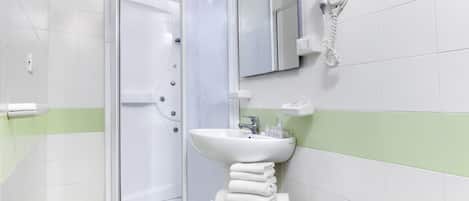 A modern bathroom with a glass-enclosed shower, a pedestal sink, and a towel stack.