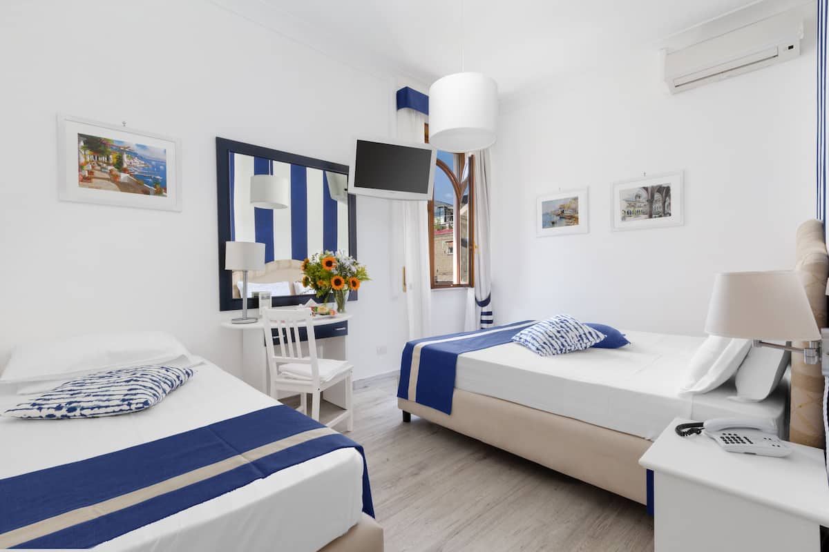A hotel room with two beds, a desk with a chair, a TV, and artwork on the walls.