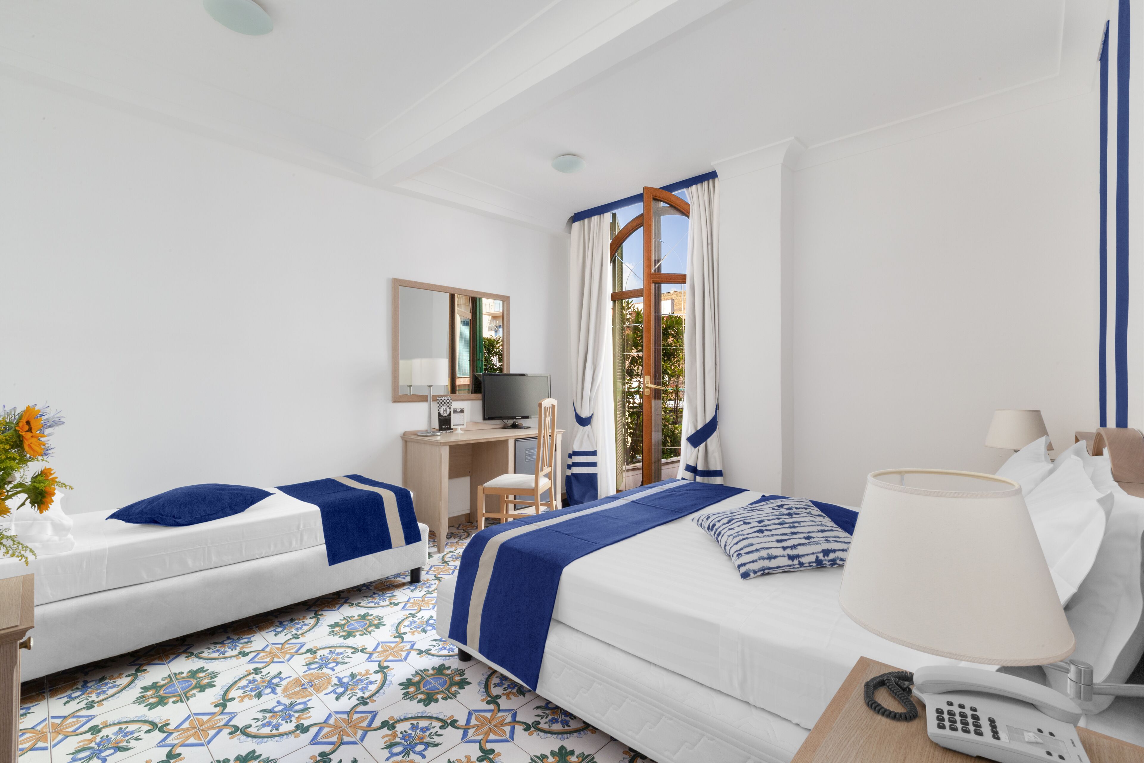 Une chambre d’hôtel avec deux lits, un bureau, une chaise, une télévision, un téléphone et une fenêtre avec des rideaux.