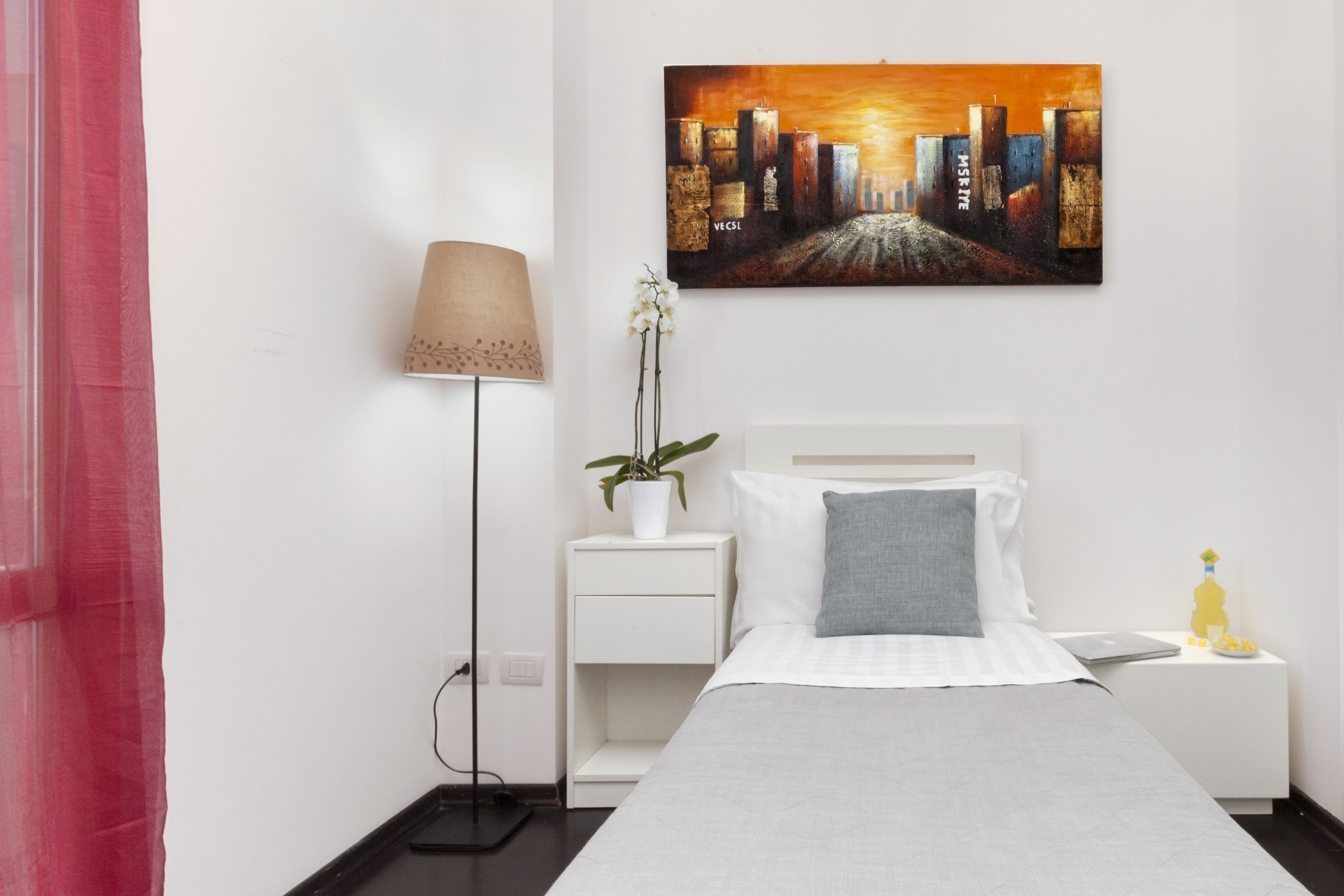 Et hotelværelse med seng, et natbord, en lampe, en potteplante og et maleri på væggen.