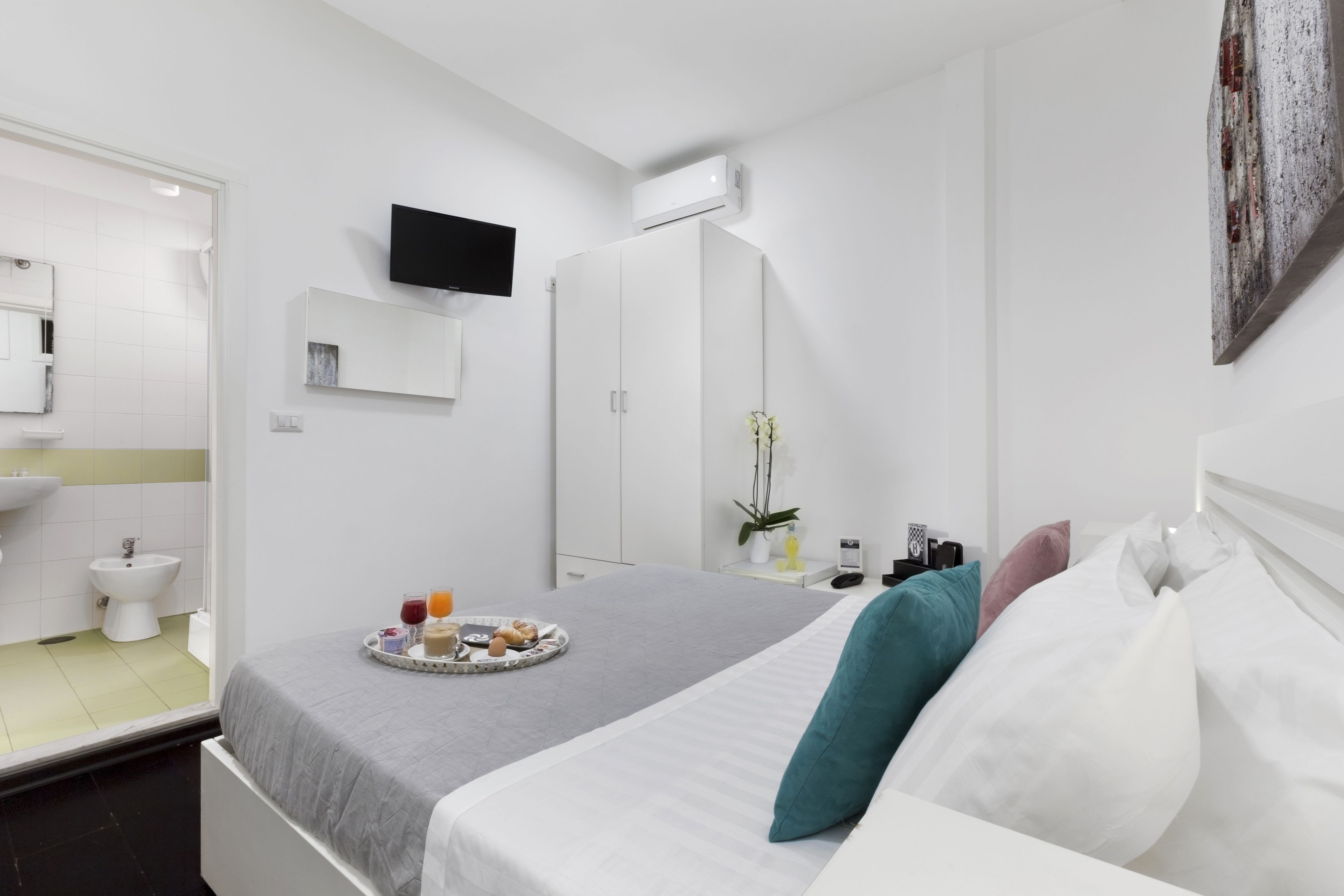 A modern hotel room with a bed, bedside table, and a small bathroom.