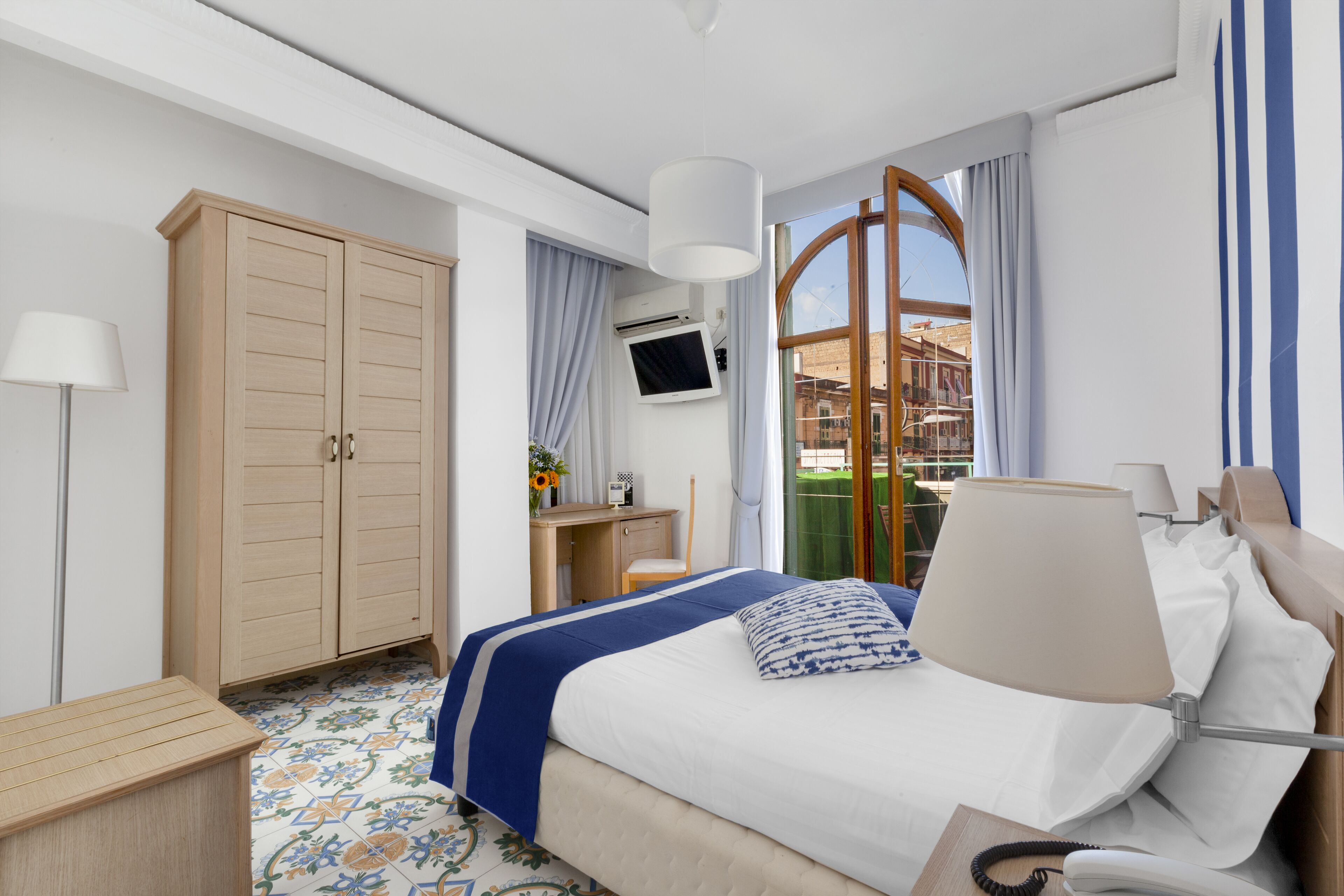 Habitación de hotel con cama, escritorio, armario, televisor y vistas al exterior.