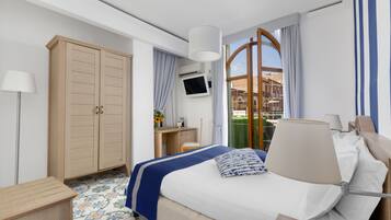 Habitación de hotel con cama, escritorio, armario, televisor y vistas al exterior.