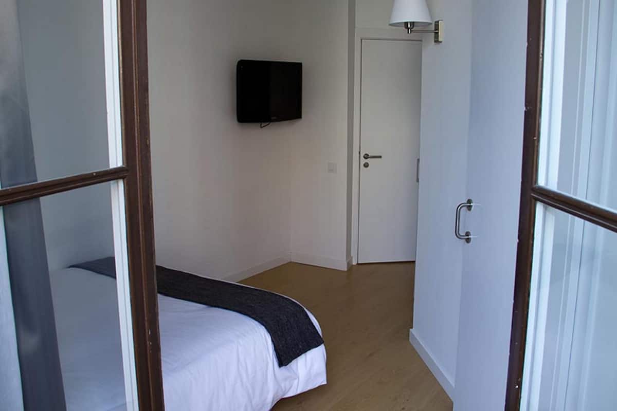 A bedroom with a bed, a television mounted on the wall, and a door with a light fixture.