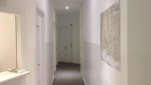 A narrow hallway with white walls, a door on the left, and a poster on the right. - Hostalin Diputacion (Barcelona)