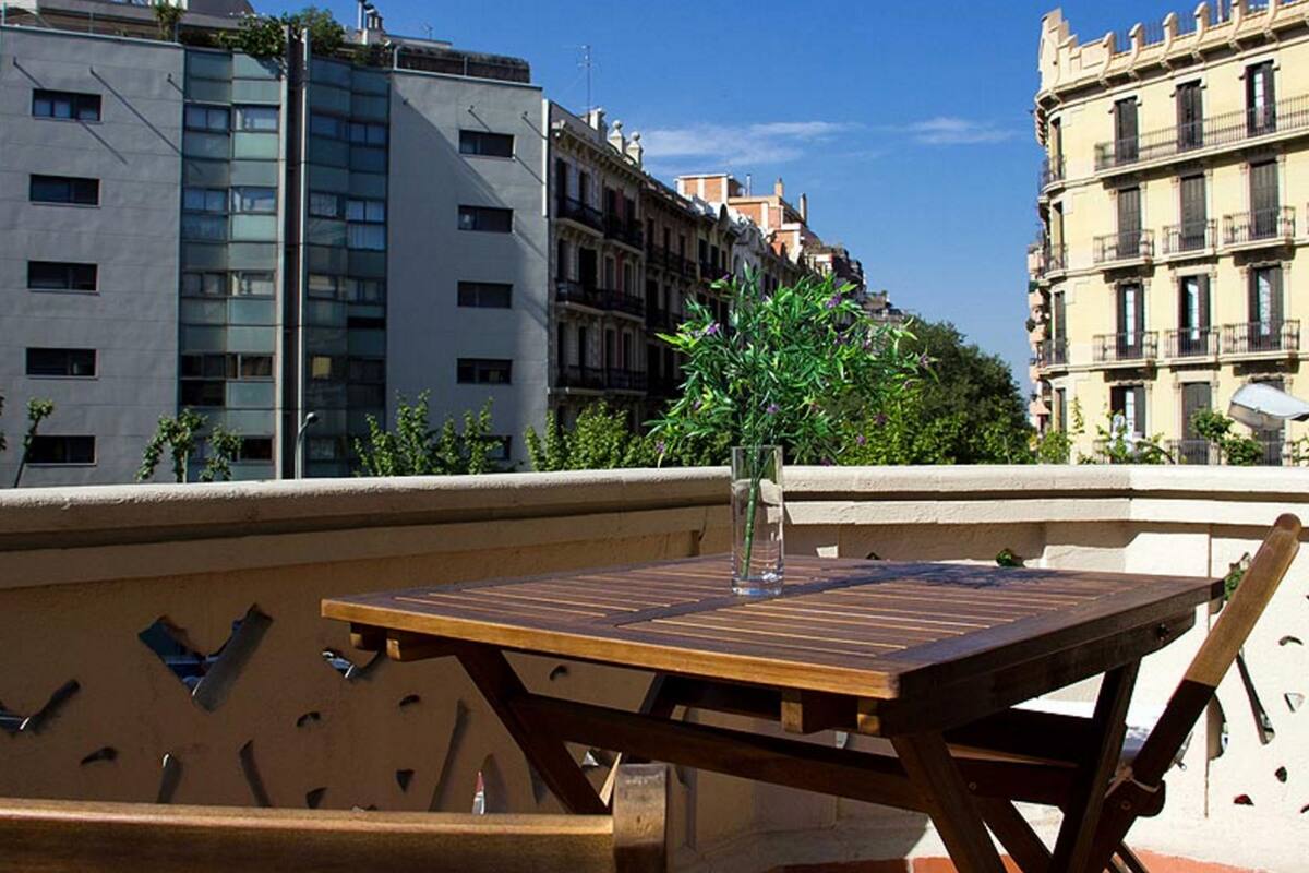 A wooden table with a glass of water and a vase of flowers on a balcony with a city view.