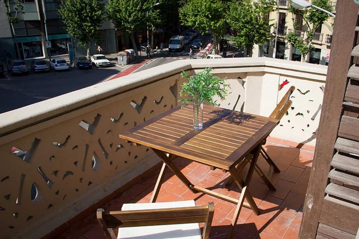 A wooden table and two chairs on a balcony with a decorative metal railing.