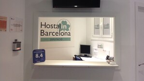 A reception desk with a sign for Hostal in Barcelona, a computer, and a flat-screen TV mounted above. - Hostalin Diputacion (Barcelona)