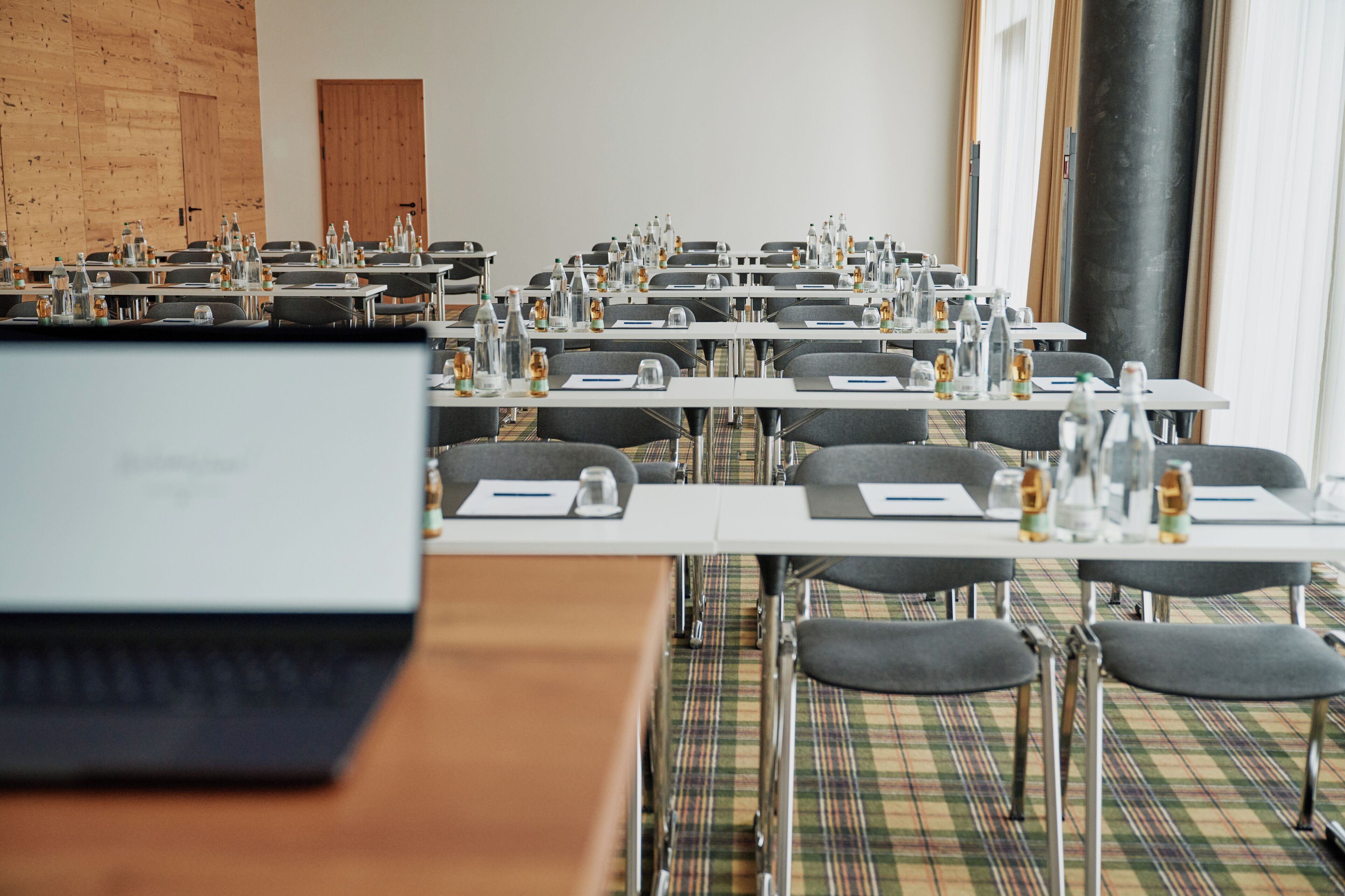 Un salón de conferencias con mesas, sillas y portátiles.