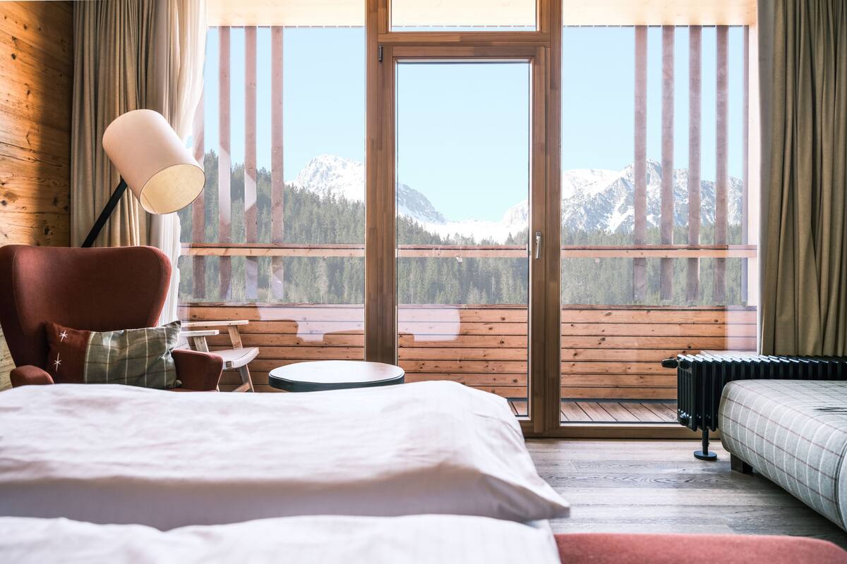Een slaapkamer met een bed, een stoel, een tafel en uitzicht op bergen door een glazen deur.