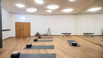 Un'ampia stanza con pavimento in legno, diversi tappetini da yoga, kettlebell e una panca.