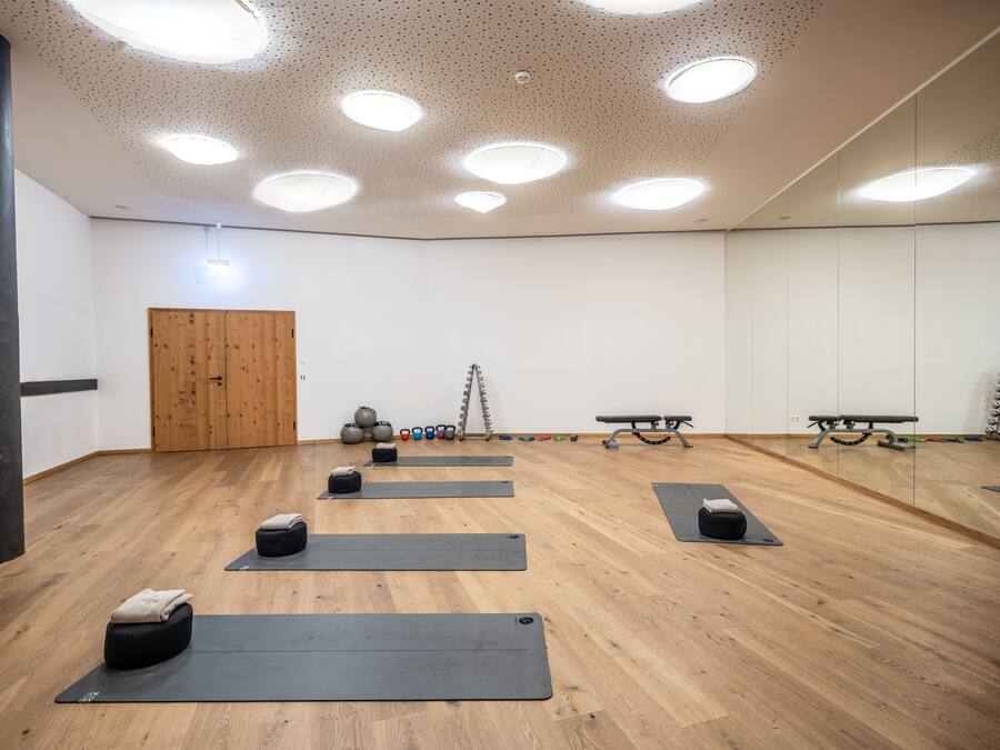 Un'ampia stanza con pavimento in legno, diversi tappetini da yoga, kettlebell e una panca.