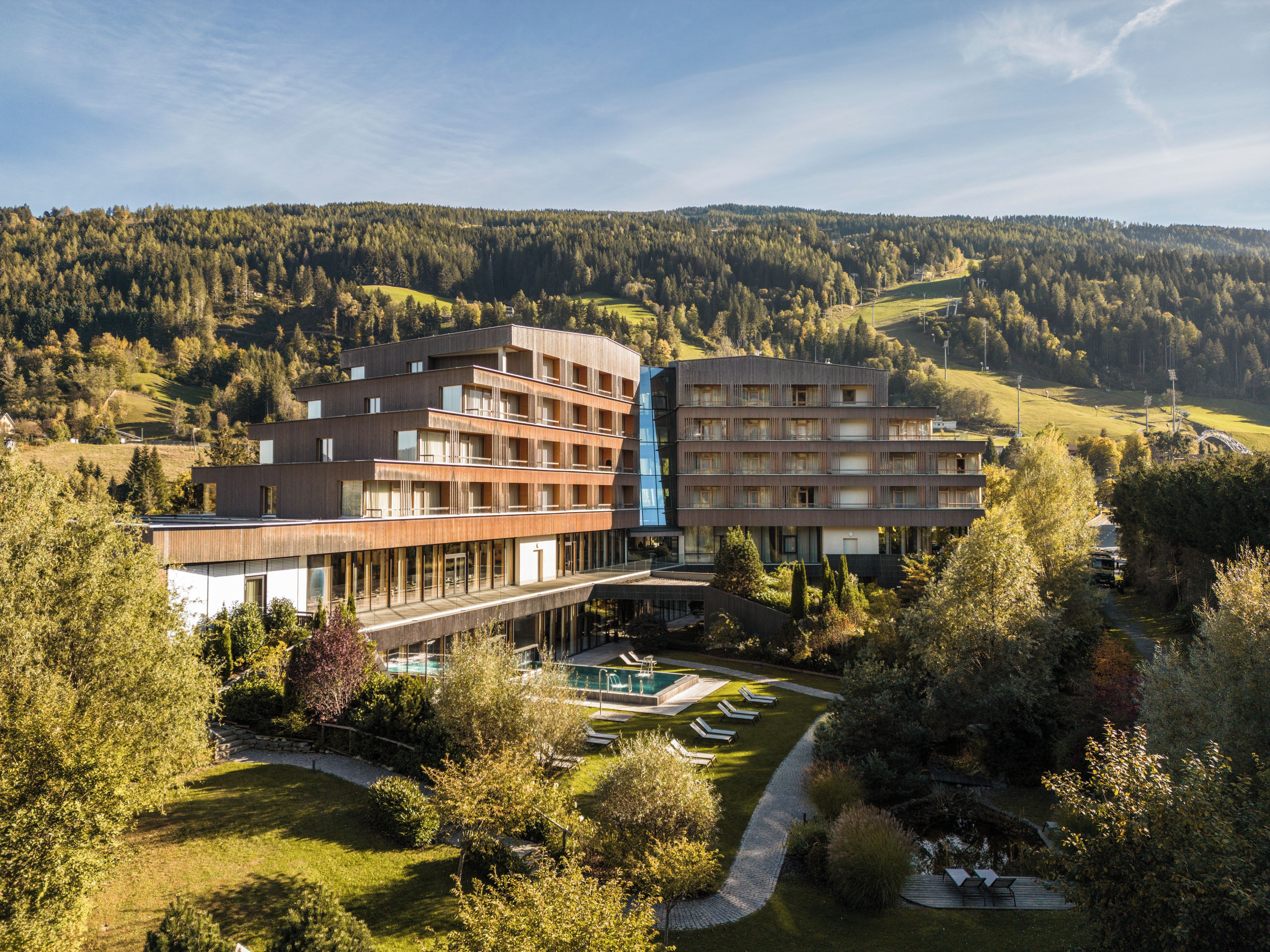 A multi-story hotel with a pool area, surrounded by lush greenery and hills.