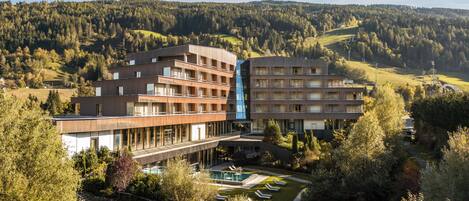 A multi-story hotel with a pool area, surrounded by lush greenery and hills.