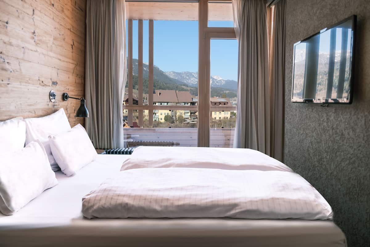 Een slaapkamer met een groot bed, houten wanden, uitzicht op bergen en een televisie aan de muur.