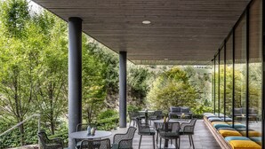 Un patio exterior con suelo de madera, mesas redondas y sillas de mimbre.