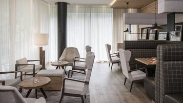 Un moderno vestíbulo de hotel con una zona de estar, una mesa a cuadros y un ventanal con cortinas translúcidas.