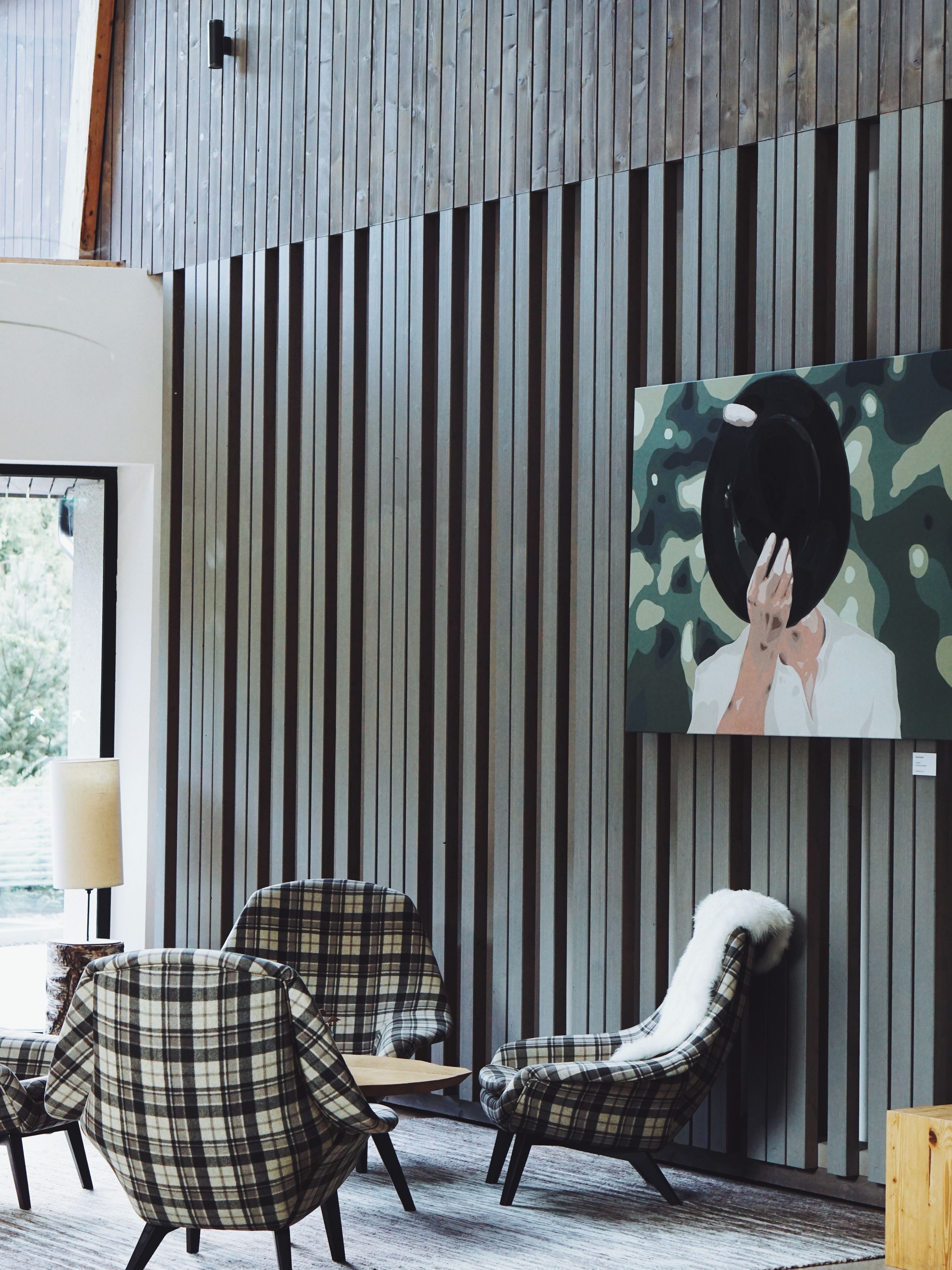 A modern interior with striped wall panels, a mounted artwork, and plaid-patterned chairs.