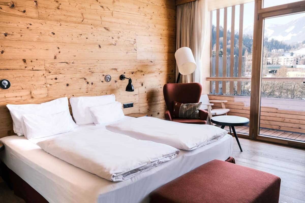 Een houten kamer met een bed, een stoel, een tafeltje en uitzicht op buiten.