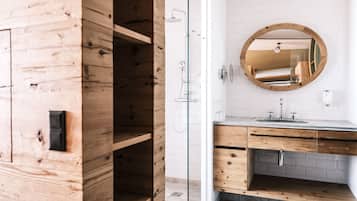 Ein modernes Badezimmer mit einem Holzbettkästchen, einem runden Spiegel und einer Duschkabine aus Glas.