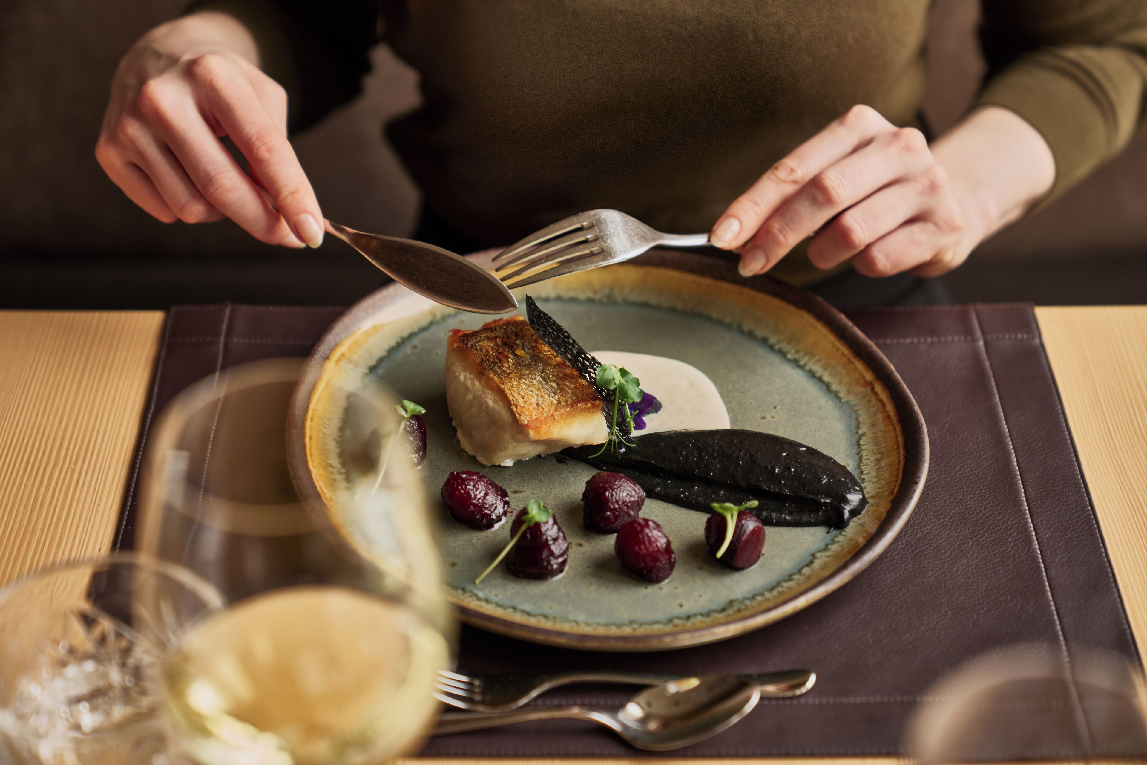 Una persona comiendo con un plato de comida, un tenedor y una cuchara sobre una mesa.
