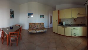 A compact living space with a dining area, sofa, kitchen, and a TV mounted on the wall. - Appartamenti Paduledda (Trinità d'Agultu e Vignola)