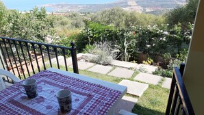 A balcony with a table set for two, overlooking a garden with a stone pathway and various plants. - Appartamenti Paduledda (Trinità d'Agultu e Vignola)