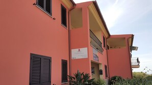 A multi-story building with a pink facade, stone base, and multiple windows with shutters. - Appartamenti Paduledda (Trinità d'Agultu e Vignola)