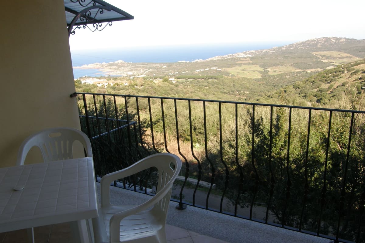 Un balcon donnant sur un paysage côtier, avec une table et deux chaises.