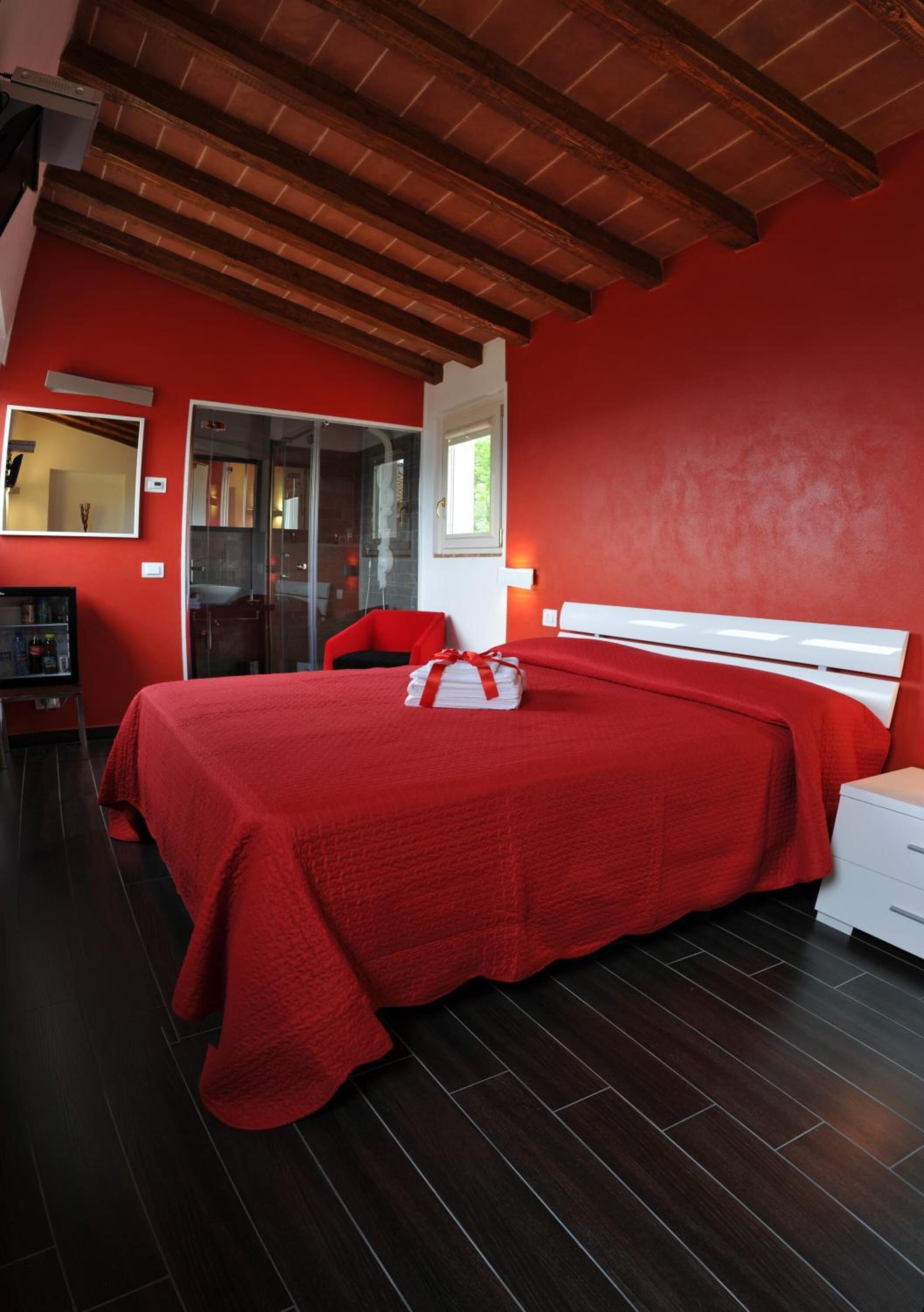 A bedroom with a red bedspread, white headboard, and a wooden ceiling.
