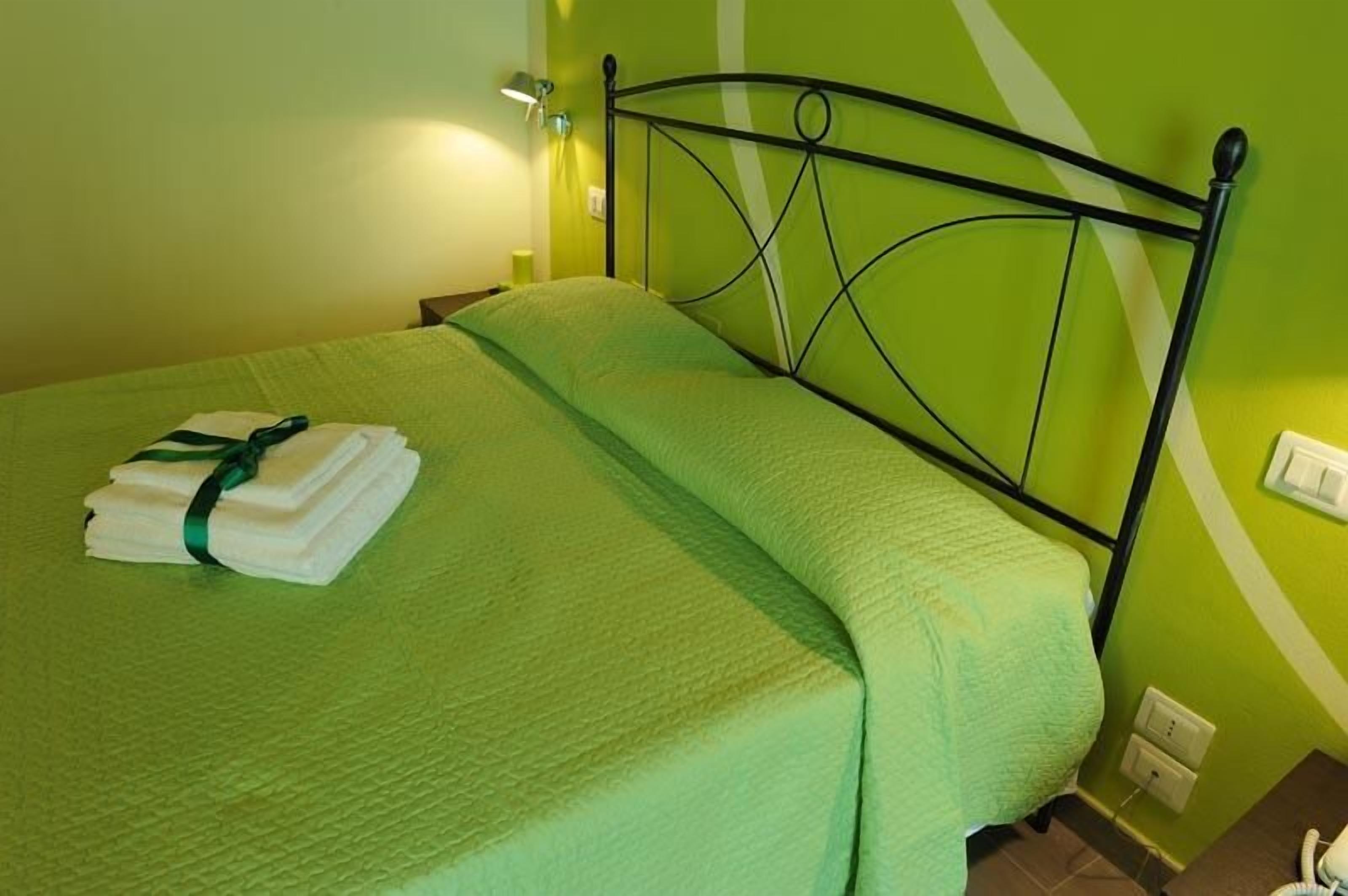Un lit recouvert d’une couverture verte et sur lequel est posée une serviette blanche soigneusement pliée, ornée d’un ruban vert.