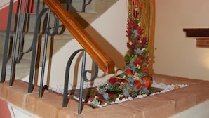 Uma escadaria com corrimão de madeira e balaústres de metal, decorada com um arranjo floral na base.