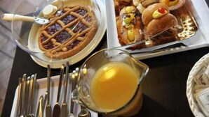 Disposição para o café da manhã com um waffle, um jarro de suco de laranja e uma bandeja de doces.