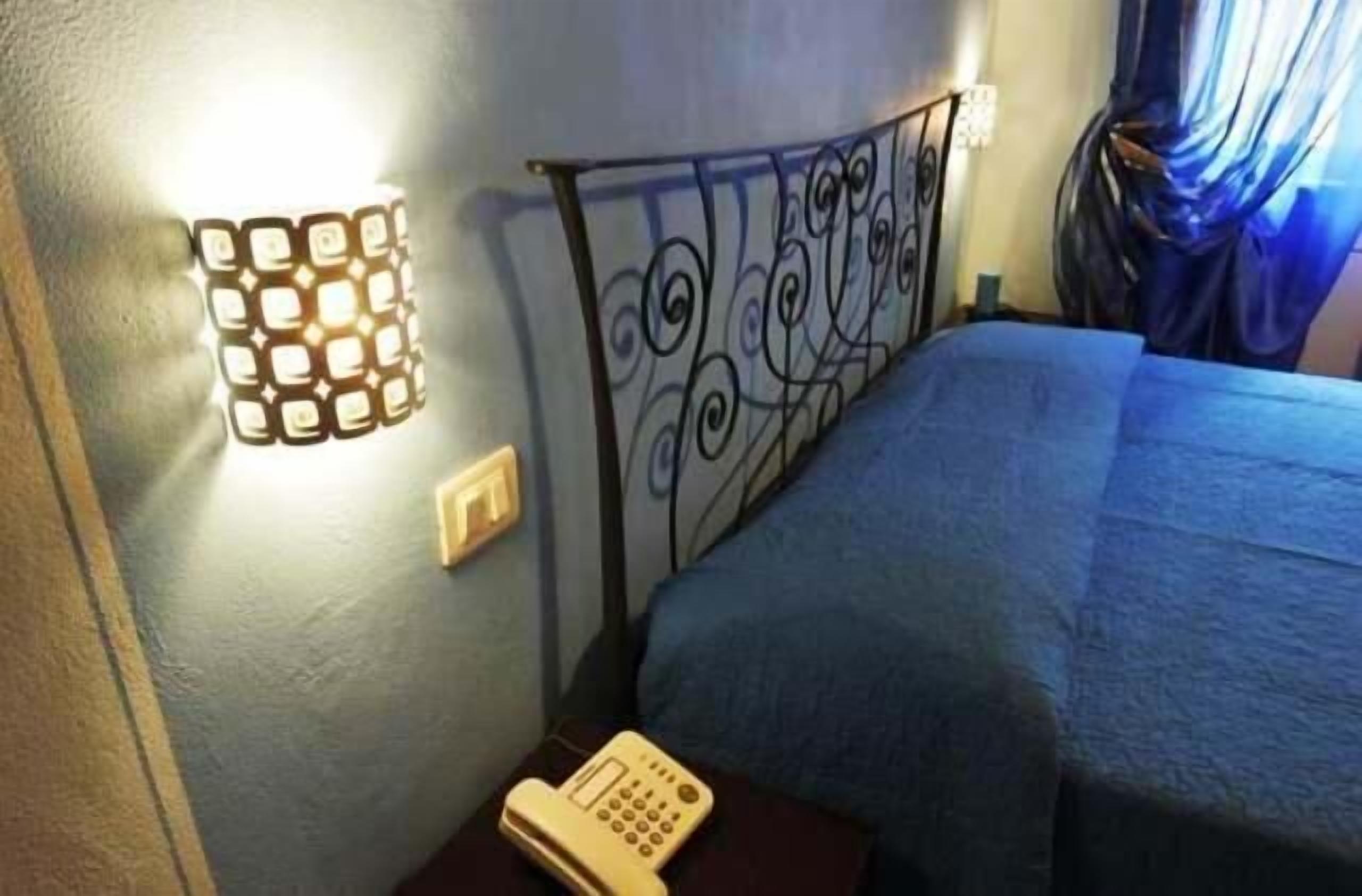 A hotel room with a bed, a nightstand, a telephone, and wall-mounted lighting.