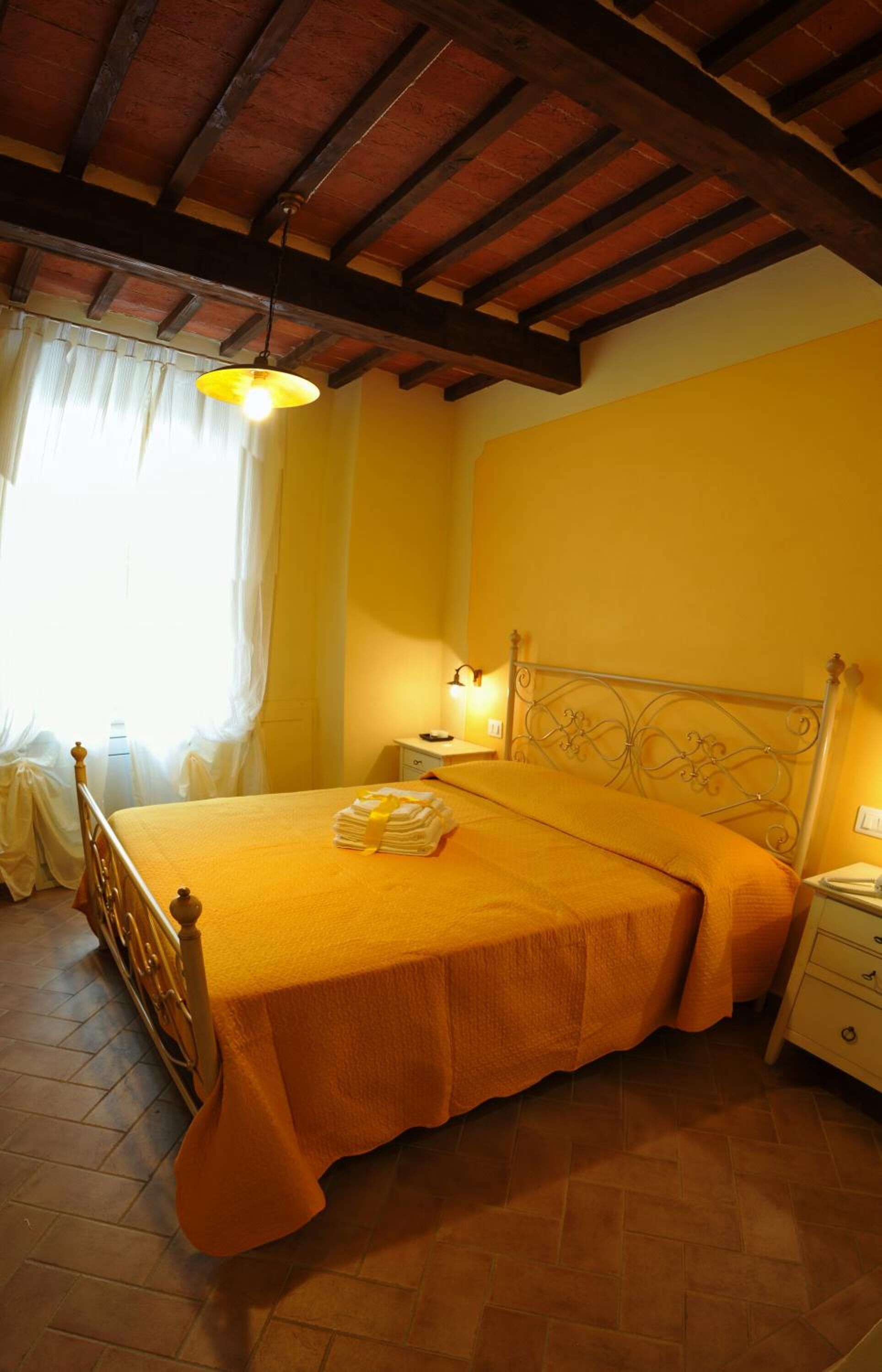 A bedroom with a wooden bed, a nightstand, a lamp, and a window with curtains.
