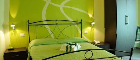 A neatly made bed with a green bedspread, two bedside tables with lamps, a wardrobe, and a wooden ceiling.
