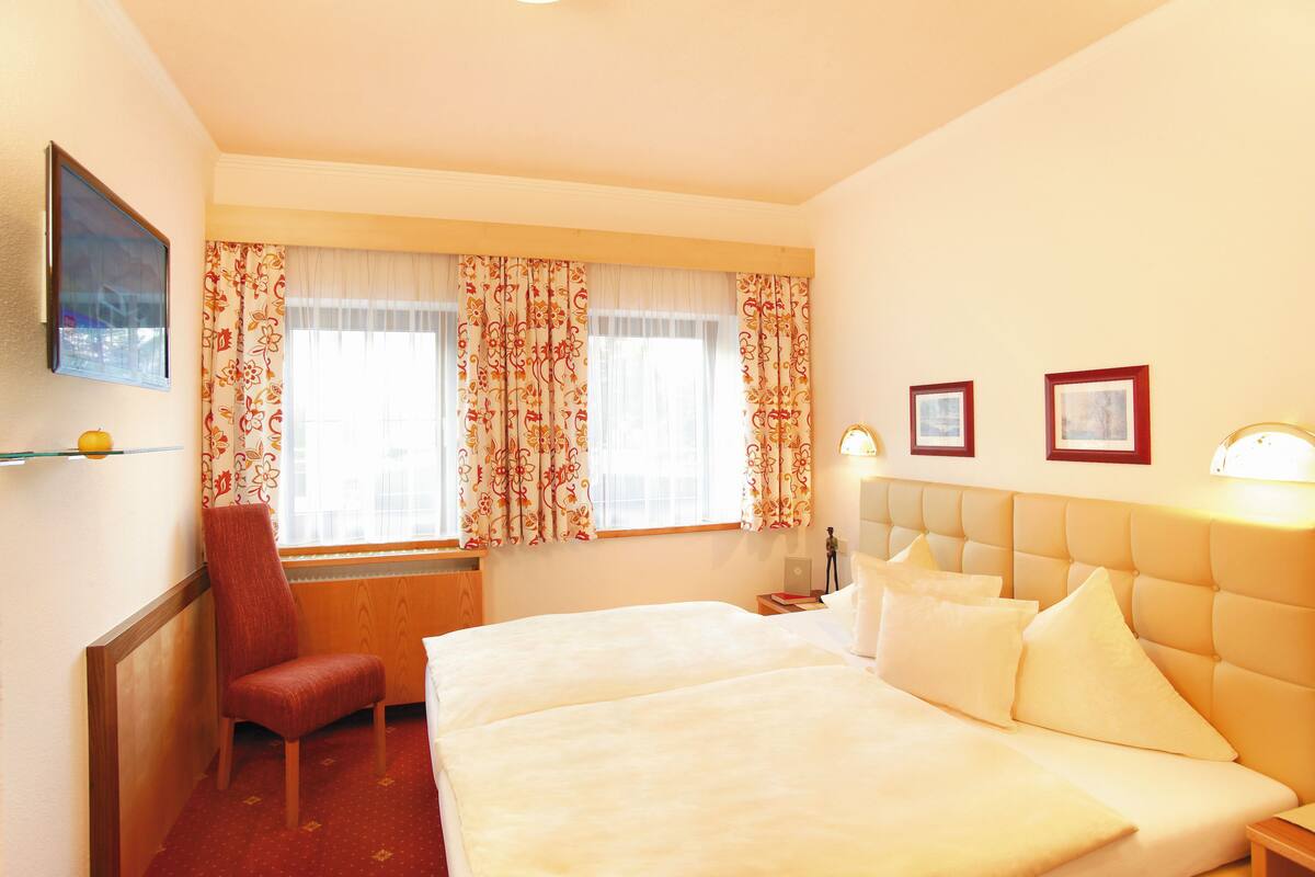 Une chambre d’hôtel avec un lit, une chaise, un bureau, une lampe et deux tableaux encadrés au mur.