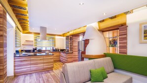 A modern kitchen with wooden cabinetry and a central island, a living area with a sofa and green cushion, and a staircase with a unique design. - Aliona Apart (Soelden)