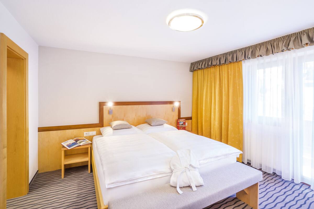 Une chambre d’hôtel avec deux lits, une tête de lit en bois, une table de chevet avec un livre et un peignoir sur le lit.