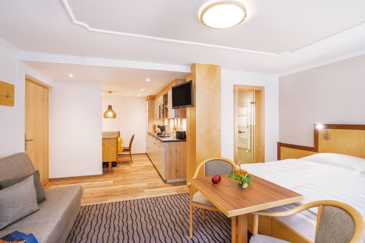 Une chambre d’hôtel comprenant un lit, une table à manger en bois, un canapé, un coin cuisine et un téléviseur.