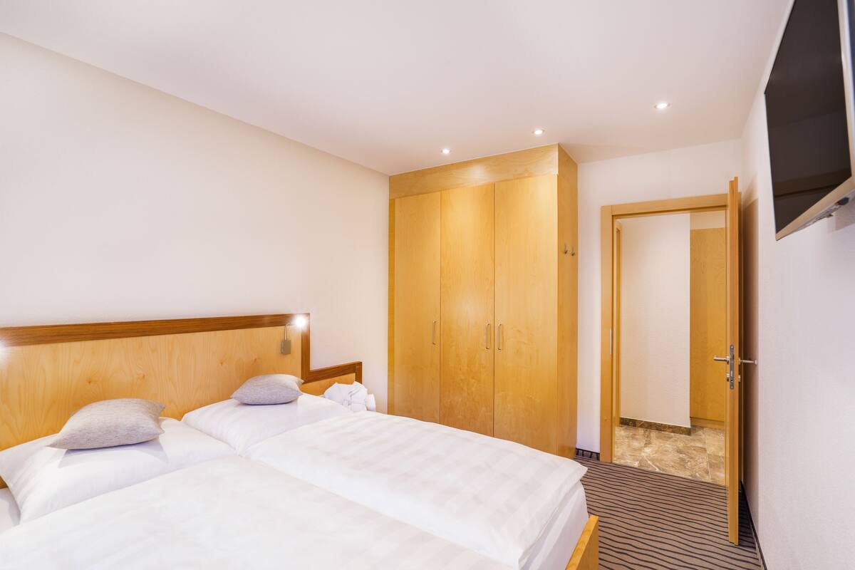 Une chambre d’hôtel avec un lit, une armoire en bois et un téléviseur fixé au mur.