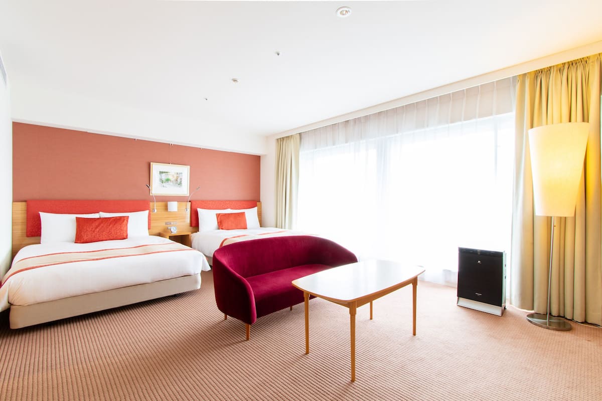 Una habitación de hotel con una cama, un sillón rojo, una mesita y una lámpara.
