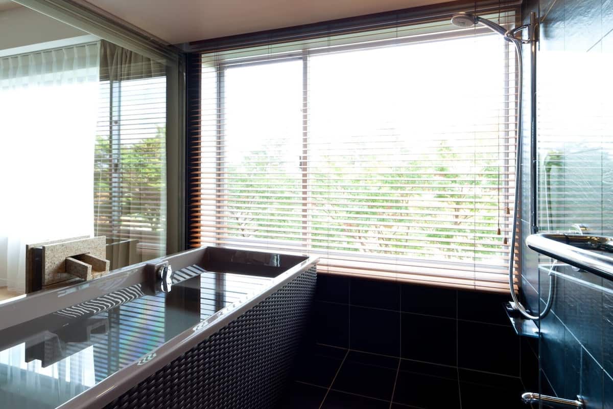 A modern bathroom with a freestanding bathtub, large windows, and a tiled floor.