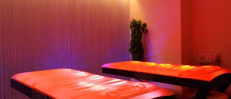 Una habitación con dos camillas de masoterapia, una planta y una pared con líneas verticales.
