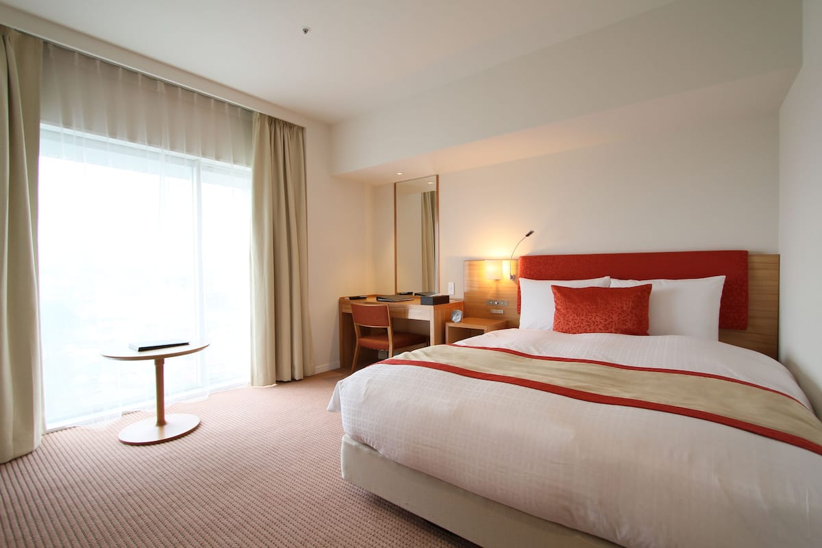 A hotel room with a large bed, a desk, a chair, and a window with curtains.