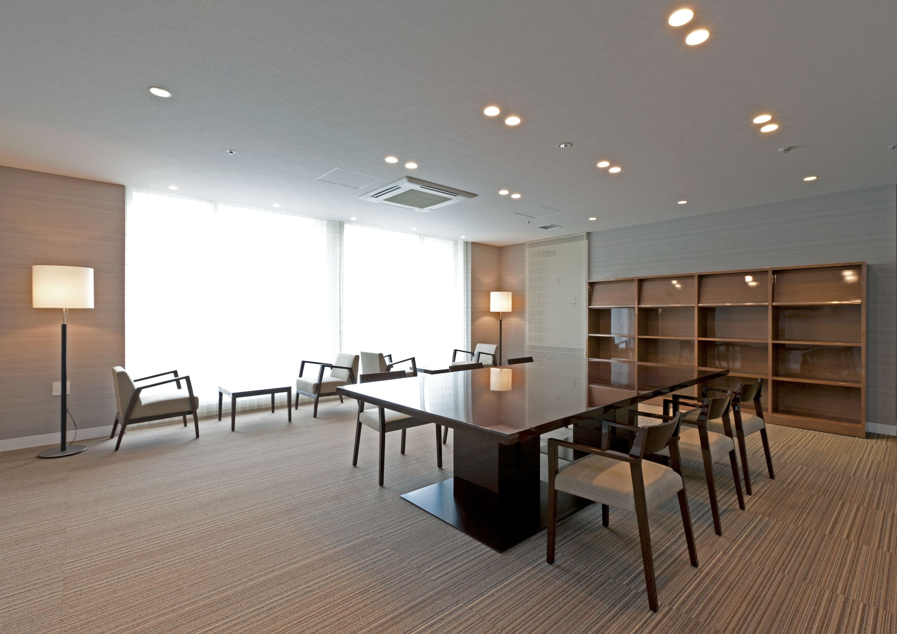 A conference room with a large table, chairs, a bookshelf, and a floor lamp.