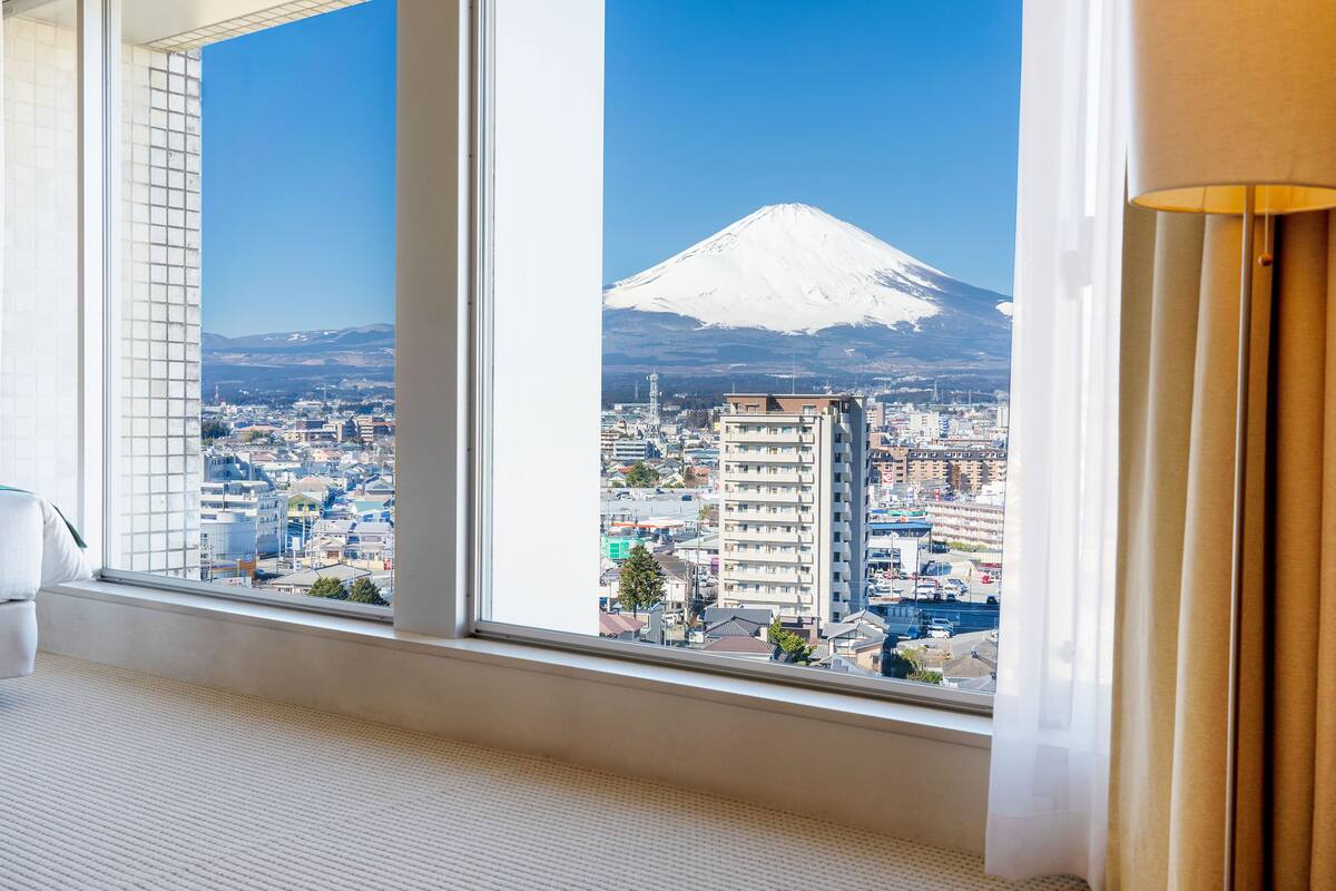 Una habitación con un amplio ventanal que da a una vista de la ciudad y una montaña nevada.