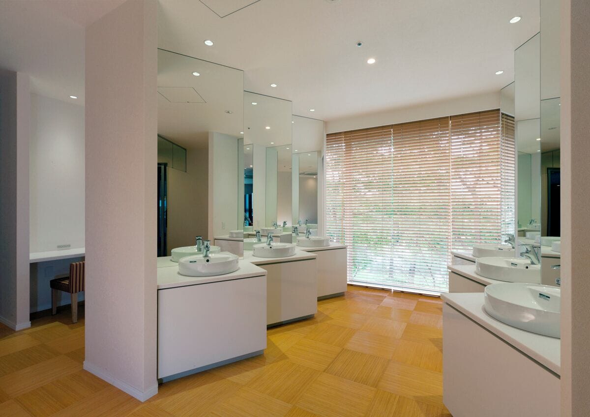 A modern bathroom with three sinks, large mirrors, and wooden blinds.