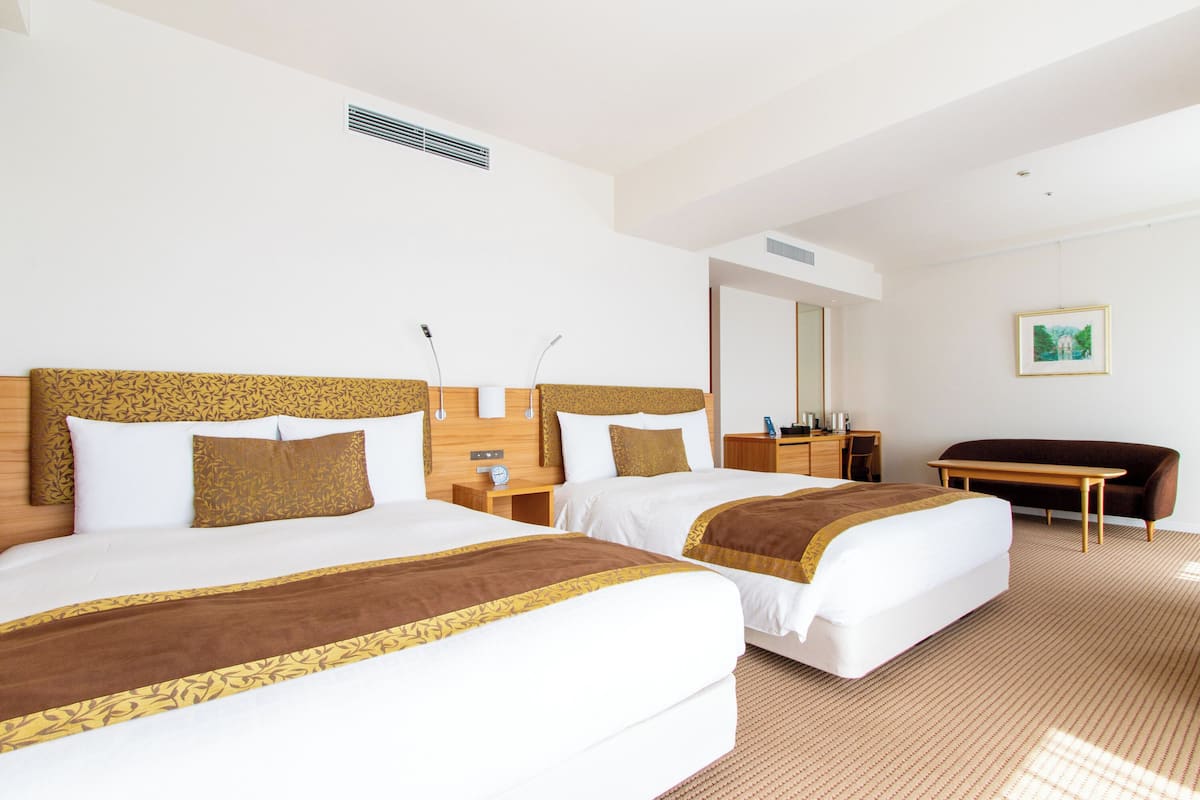 Una habitación de hotel con dos camas, un escritorio, una silla y un espejo grande.