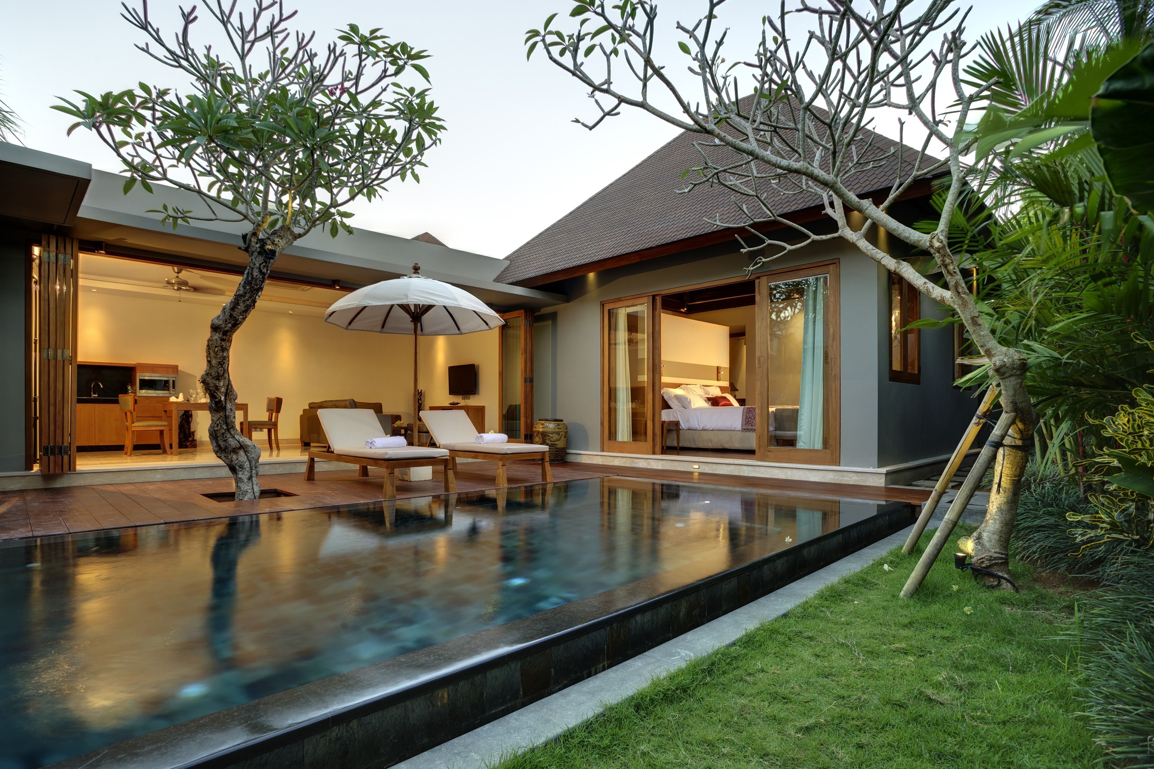 A modern house with a swimming pool, two lounge chairs, a dining area, and a large sliding glass door leading to a bedroom.